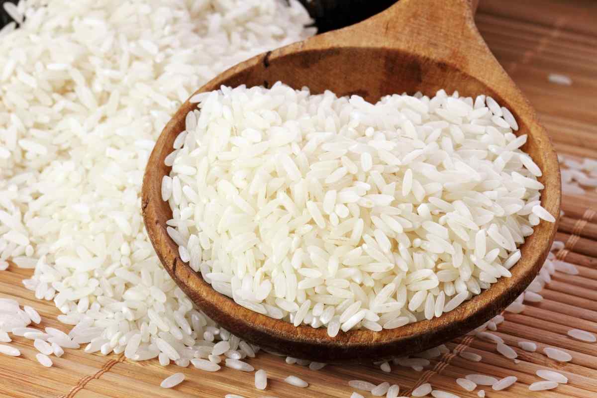 Polished white rice grains heaped in a wooden spoon beside spilled rice
