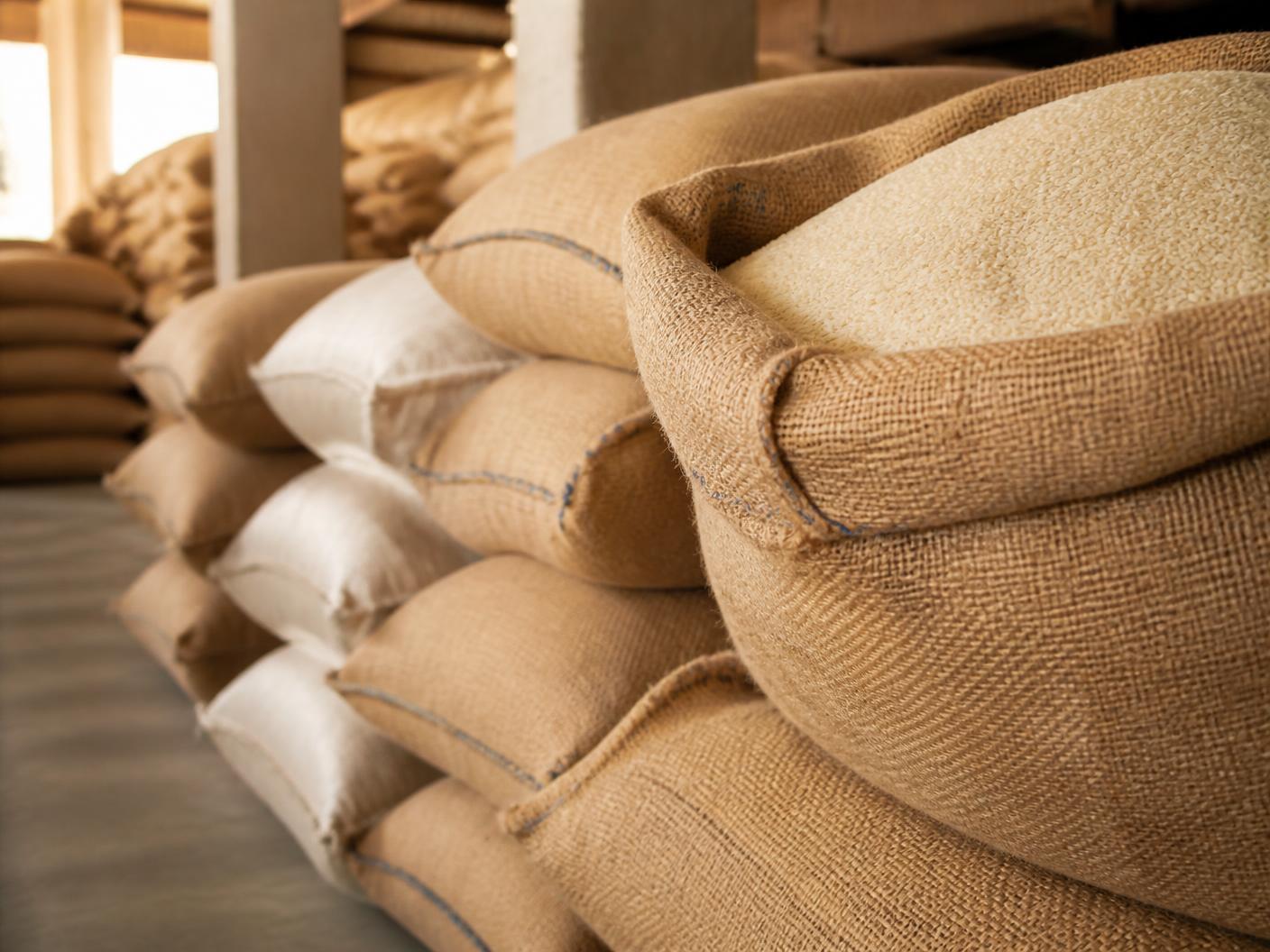 Stacked jute and woven sacks of rice in a warm-lit warehouse