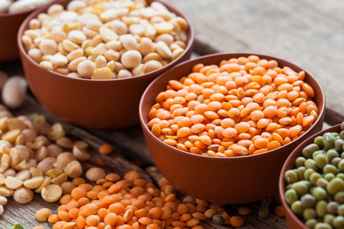Clay bowls of red lentils, split peas and green moong on a wooden table